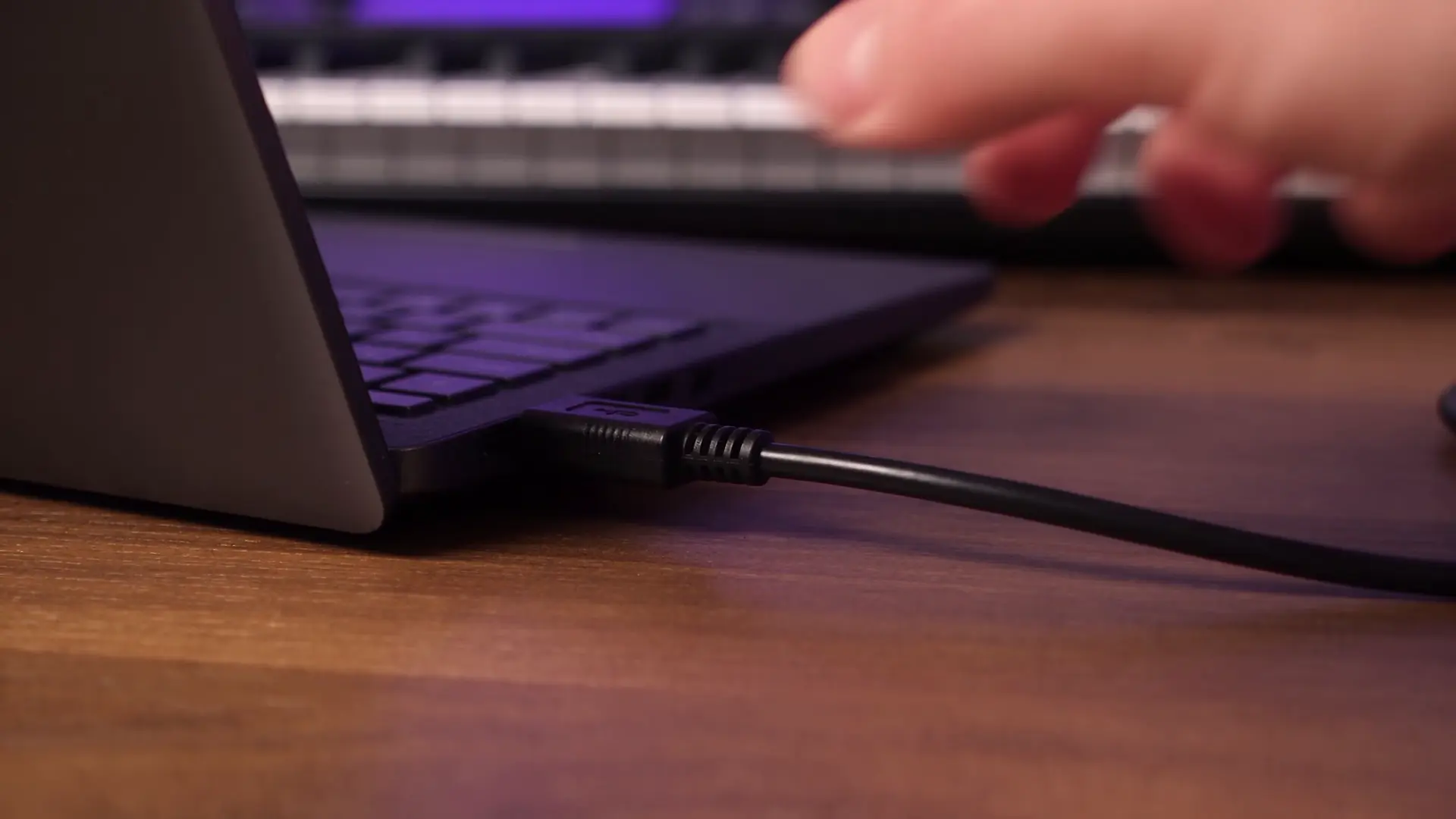 Un câble USB se branchant sur un ordinateur portable, puis un musicien jouant sur un clavier MIDI